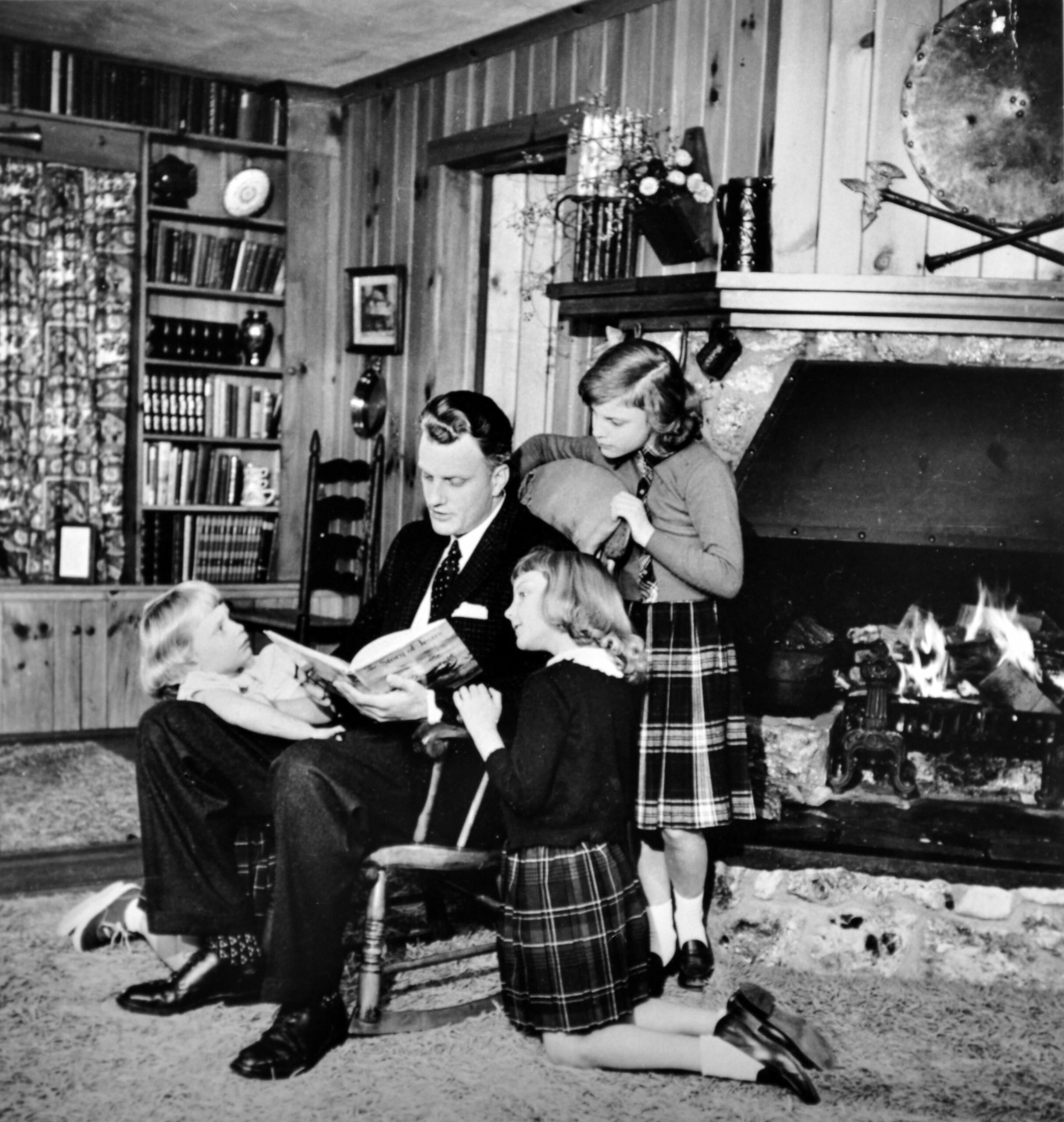 a father reading aloud to his daughters beside the fireplace
